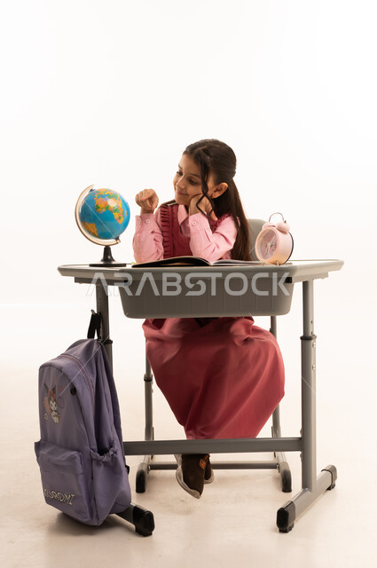 أهمية التعليم في بناء مستقبل مشرق للمجتمع ، مفهوم البحث والإستكشاف حول العالم، بورتريه لطالبة عربية خليجية سعودية ترتدي الزي المدرسي تجلس على طاوله مكتبية تقوم بمذاكره الدروس المدرسيه، خلفية بيضاء