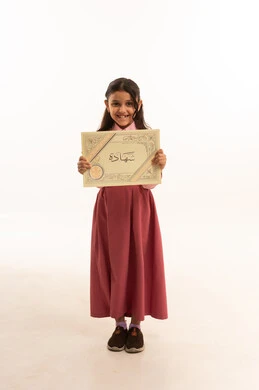 النجاح وانتهاء العام الدراسي، مفهوم التفوق والتخرج من المدرسة, النظر الى الكاميرا بايماءات الفخر والسعاده, جودة التعليم في السعوديه, بورتريه  لطالبة عربية سعودية خليجية مبتسمة ترتدي الزي المدرسي تمسك بيدها الشهادة، الجسم بالطول الكامل، خلفية بيضاء