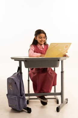 End of the school year, concept of excellence, success and graduation from school, looking at the camera with gestures of pride and happiness, quality of education in Saudi Arabia, portrait of a smiling Saudi Arabian Gulf student wearing school uniform sitting at her desk holding her certificate, white background