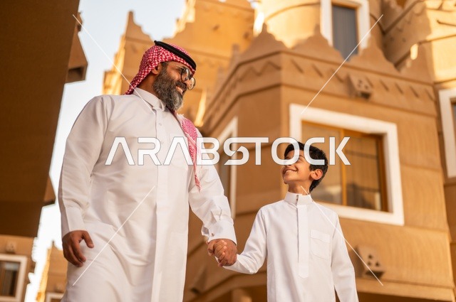 A family atmosphere filled with affection, a close-up image of a family standing at the entrance of a modern home, a child wearing a white dress, having a good time with the children, sharing happy moments and fun with the kids, an Arab Gulf Saudi father holding his son's hand and playing with him, enjoying playing with the family, the concept of a happy family.