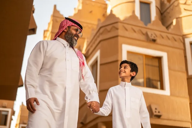 أجواء أسرية مليئة بالمودة، صورة مقربة لعائلة تقف عند مدخل منزل عصري ، طفل يرتدي الثوب الأبيض، قضاء وقت ممتع مع الأطفال, مشاركة اللحظات السعيدة والتسلية مع الأبناء,أب عربي خليجي سعودي يمسك بيد ابنه ويلعب معه, الاستمتاع باللعب مع العائلة، مفهوم الأسرة السعيدة