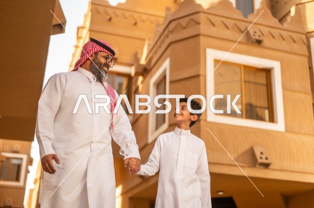 الاستمتاع باللعب مع العائلة، أجواء أسرية مليئة بالمودة، عائلة تقف عند مدخل منزل عصري ، طفل يرتدي الثوب الأبيض، قضاء وقت ممتع مع الأطفال, مشاركة اللحظات السعيدة والتسلية مع الأبناء,أب عربي خليجي سعودي يمسك بيد ابنه ويلعب معه, مفهوم الأسرة السعيدة