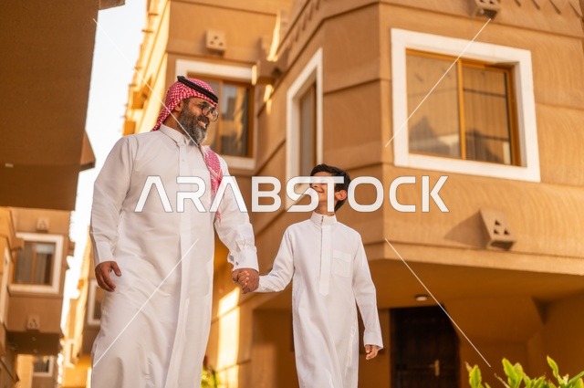 أجواء أسرية مليئة بالمودة، صورة مقربة لعائلة تقف عند مدخل منزل عصري ، طفل يرتدي الثوب الأبيض، قضاء وقت ممتع مع الأطفال, مشاركة اللحظات السعيدة والتسلية مع الأبناء,أب عربي خليجي سعودي يمسك بيد ابنه ويلعب معه, الاستمتاع باللعب مع العائلة، مفهوم الأسرة السعيدة