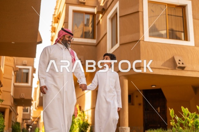 مفهوم الأسرة السعيدة، عائلة تقف عند مدخل منزل عصري ،طفل يرتدي الثوب الأبيض، قضاء وقت ممتع مع الأطفال, مشاركة اللحظات السعيدة والتسلية مع الأبناء,أب عربي خليجي سعودي يمسك بيد ابنه ويلعب معه, الاستمتاع باللعب مع العائلة