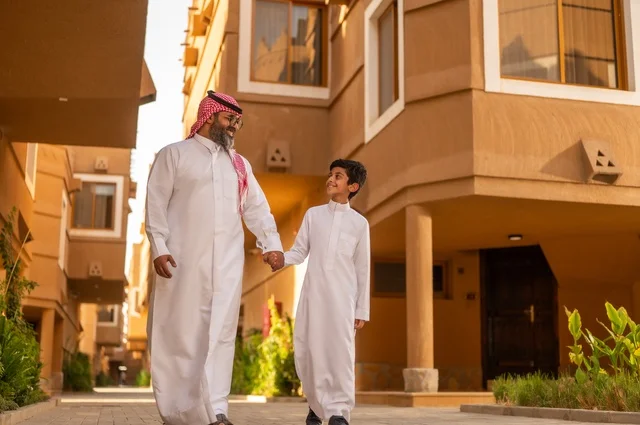 ايماءات وجه وايدي تعبر عن المحبة، أجواء أسرية مليئة بالمودة، عائلة تقف عند مدخل منزل عصري ، طفل يرتدي الثوب الأبيض، قضاء وقت ممتع مع الأطفال, مشاركة اللحظات السعيدة والتسلية مع الأبناء,أب عربي خليجي سعودي يمسك بيد ابنه ويلعب معه, مفهوم الأسرة السعيدة