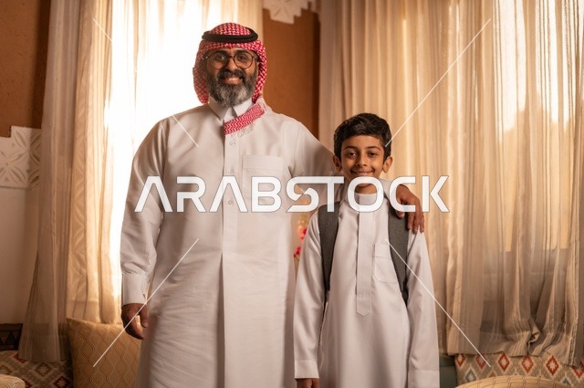 نظرات مليئة بالحب والحنان، مفهوم الأبوة والاعتناء بالأبناء, عائلة تنظر إلى الكاميرا داخل مجلس تراثي بديكورات وزخارف تقليدية، أب عربي خليجي سعودي يرتدي الثوب التقليدي والغتره يضع يده على كتف ولده ويقدم له بعض النصائح المفيدة، التنزه وقضاء الوقت مع العائلة