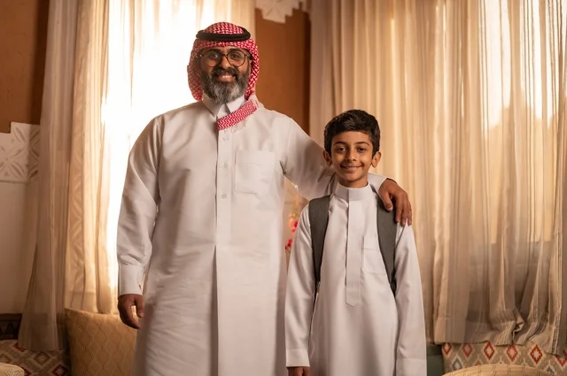 نظرات مليئة بالحب والحنان، مفهوم الأبوة والاعتناء بالأبناء, عائلة تنظر إلى الكاميرا داخل مجلس تراثي بديكورات وزخارف تقليدية، أب عربي خليجي سعودي يرتدي الثوب التقليدي والغتره يضع يده على كتف ولده ويقدم له بعض النصائح المفيدة، التنزه وقضاء الوقت مع العائلة