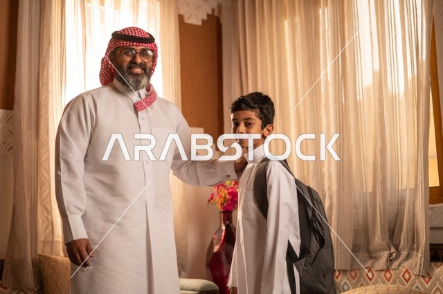 نظرات مليئة بالحب والحنان، مفهوم الأبوة والاعتناء بالأبناء, عائلة تنظر إلى الكاميرا داخل مجلس تراثي بديكورات وزخارف تقليدية، أب عربي خليجي سعودي يرتدي الثوب التقليدي والغتره يضع يده على كتف ولده ويقدم له بعض النصائح المفيدة، التنزه وقضاء الوقت مع العائلة