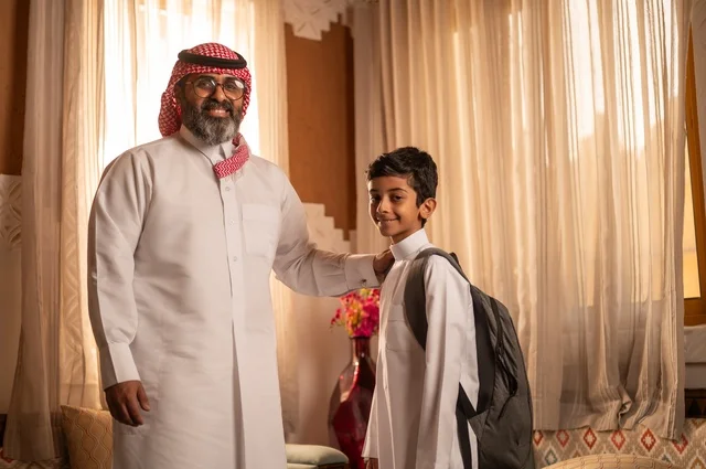 نظرات مليئة بالحب والحنان، مفهوم الأبوة والاعتناء بالأبناء, عائلة تنظر إلى الكاميرا داخل مجلس تراثي بديكورات وزخارف تقليدية، أب عربي خليجي سعودي يرتدي الثوب التقليدي والغتره يضع يده على كتف ولده ويقدم له بعض النصائح المفيدة، التنزه وقضاء الوقت مع العائلة