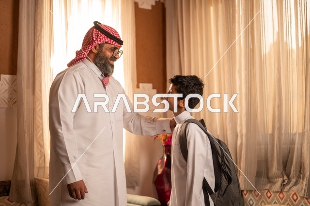 لحظات عائلية سعيدة، مفهوم الأبوة والاعتناء بالأبناء, عائلة تقف داخل مجلس تراثي بديكورات وزخارف تقليدية، أب عربي خليجي سعودي يرتدي الثوب التقليدي والغتره ويضع يده على كتف ولده، نظرات مليئة بالحب والحنان، التنزه وقضاء الوقت مع العائلة