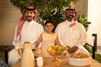 Kinship ties and family bonds, children's joy and happiness during the happy Eid days, family gatherings and visits during Islamic holidays and occasions, a Saudi Arabian Gulf man wearing traditional clothing sitting with his grandchildren with gestures of joy and happiness, Eid hospitality and sweets, good reception and hospitality of the guest