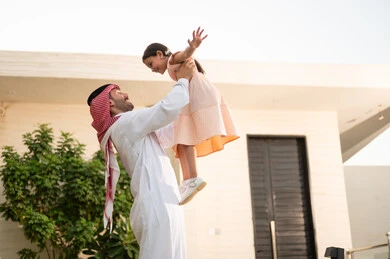 قضاء أوقات ممتعه مع الأهل الأبناء، رجل عربي خليجي سعودي يرتدي الثوب التقليدي والشماغ يرفع ابنته عاليا بإيماءات السعادة، المحافظة على الترابط الأسري، الاعتناء والاهتمام بالاولاد، اللعب والتسلية والترفيه مع العائلة في الهواء الطلق