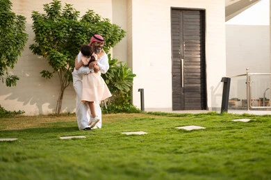 Playing, having fun and entertaining with the family outdoors, spending quality time with parents and children, a Saudi Arabian Gulf man wearing traditional thobe and shemagh playing in the garden with his daughter with happy gestures, maintaining family ties, taking care of and looking after the children