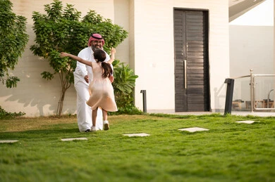 Playing, having fun and entertaining with the family outdoors, spending quality time with parents and children, a Saudi Arabian Gulf man wearing traditional thobe and shemagh playing in the garden with his daughter with happy gestures, maintaining family ties, taking care of and looking after the children