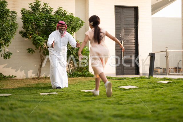  اللعب والتسلية والترفيه مع العائلة في الهواء الطلق, قضاء أوقات ممتعه مع الأهل الأبناء، رجل عربي خليجي سعودي يرتدي الثوب التقليدي والشماغ يلعب في الحديقة مع ابنته بإيماءات السعادة، المحافظة على الترابط الأسري، الاعتناء والاهتمام بالاولاد