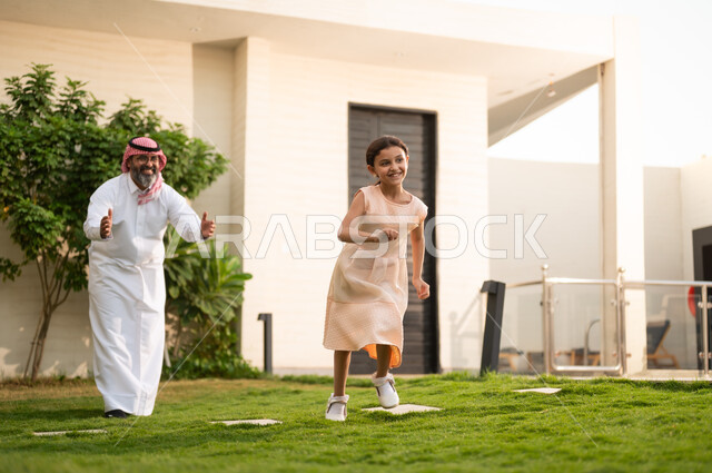  اللعب والتسلية والترفيه مع العائلة في الهواء الطلق, قضاء أوقات ممتعه مع الأهل الأبناء، رجل عربي خليجي سعودي يرتدي الثوب التقليدي والشماغ يلعب في الحديقة مع ابنته بإيماءات السعادة، المحافظة على الترابط الأسري، الاعتناء والاهتمام بالاولاد