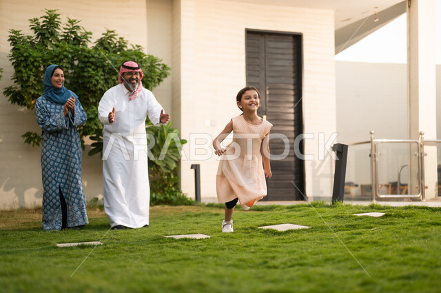  المحافظة على الترابط الأسري، الاعتناء والاهتمام بالاولاد, اللعب والتسلية والترفيه مع العائلة في الهواء الطلق, قضاء أوقات ممتعه مع الأهل الأبناء، زوجان عربيان خليجيان سعوديان يلعبان في الحديقة مع ابنتهما بإيماءات السعادة