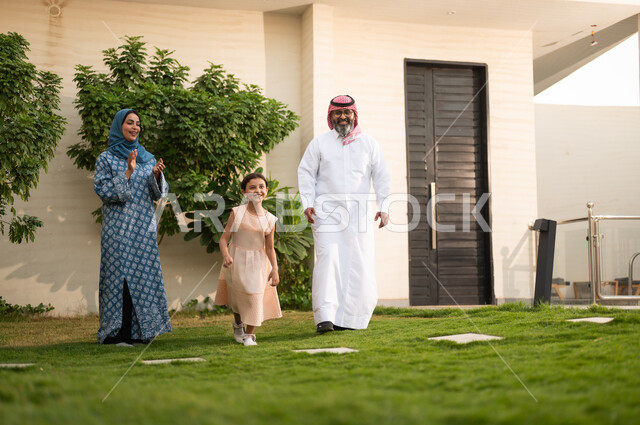 Maintaining family ties, taking care of the children, playing, having fun and entertaining with the family outdoors, spending quality time with parents and children, a Saudi Arabian Gulf couple playing in the garden with their daughter with happy gestures
