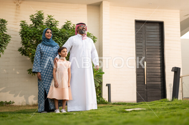 Maintaining family ties, taking care of the children, playing, having fun and entertaining with the family outdoors, spending quality time with parents and children, a Saudi Arabian Gulf couple playing in the garden with their daughter with happy gestures