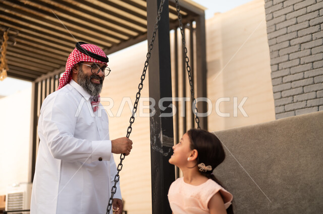  التأرجح على الأرجوحه, الإستمتاع باللعب في يوم مشمس, قضاء وقت ممتع في الخارج، فتاة عربيه سعوديه خليجيه مبتسمة تلعب في المنتزه بتعابير السرور والسعادة برفقة والدها