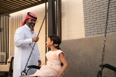  التأرجح على الأرجوحه, الإستمتاع باللعب في يوم مشمس, قضاء وقت ممتع في الخارج، فتاة عربيه سعوديه خليجيه مبتسمة تلعب في المنتزه بتعابير السرور والسعادة برفقة والدها