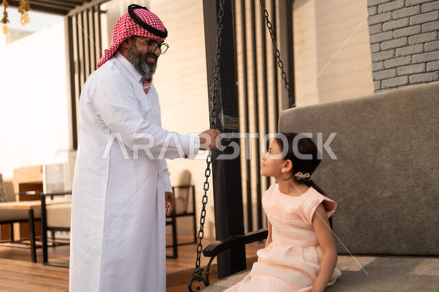 الإستمتاع باللعب في يوم مشمس, قضاء وقت ممتع في الخارج، فتاة عربيه سعوديه خليجيه مبتسمة تلعب في المنتزه بتعابير السرور والسعادة برفقة والدها, التأرجح على الأرجوحه