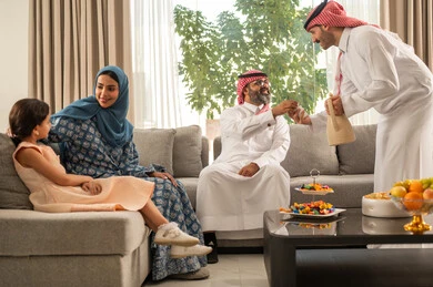 Eid hospitality and sweets, good reception and hospitality of guests, kinship and family ties, joy and happiness of children during the happy Eid days, family gatherings and visits during Islamic holidays and occasions, an Arab Gulf Saudi man wearing traditional clothes sitting with his grandchildren with gestures of joy and happiness