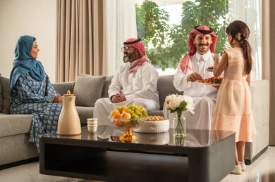 حسن استقبال وإكرام الضيف، صلة الرحم والترابط الاسري, فرحة وبهجة الابناء في ايام العيد السعيد, التجمعات والزيارات الاسرية في الأعياد والمناسبات الاسلامية, رجل عربي خليجي سعودي يرتدي الثوب التقليدي يجلس مع أحفاده بإيماءات الفرح والسرور, ضيافة وحلوى العيد