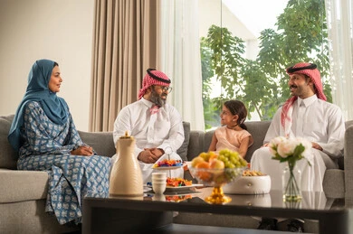 Welcoming and honoring guests, maintaining family ties and cohesion, children's joy and happiness during Eid, family gatherings and visits during Islamic holidays and occasions, a Saudi Arabian Gulf man wearing traditional clothing sitting with his grandchildren with gestures of joy and happiness, Eid hospitality and sweets