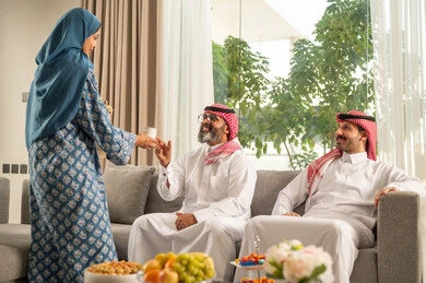 حسن استقبال وإكرام الضيف، صلة الرحم والترابط الاسري, فرحة وبهجة الابناء في ايام العيد السعيد, التجمعات والزيارات الاسرية في الأعياد والمناسبات الاسلامية, رجل عربي خليجي سعودي يرتدي الثوب التقليدي يجلس مع أحفاده بإيماءات الفرح والسرور, ضيافة وحلوى العيد
