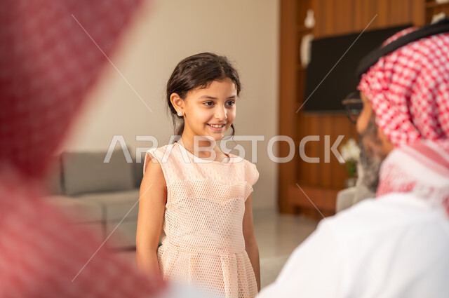 تقديم العيدية في العيد، مفهوم الحب والحنان، دور الأب في حياه الأبناء، جد عربي خليجي سعودي يرتدي الثوب التقليدي والشماغ يجلس على كرسي يعطي الفلوس لحفيدته، عادات وتقاليد الاعياد والمناسبات الدينية، ايماءات السعادة والسرور،  اجواء اسرية مليئة بالفرح