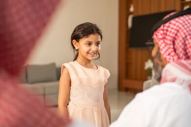 تقديم العيدية في العيد، مفهوم الحب والحنان، دور الأب في حياه الأبناء، جد عربي خليجي سعودي يرتدي الثوب التقليدي والشماغ يجلس على كرسي يعطي الفلوس لحفيدته، عادات وتقاليد الاعياد والمناسبات الدينية، ايماءات السعادة والسرور،  اجواء اسرية مليئة بالفرح