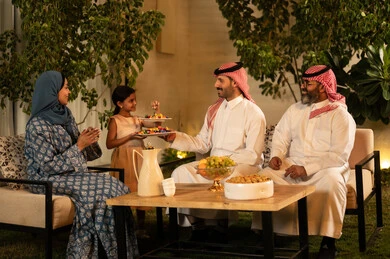 صلة الرحم والترابط الاسري, فرحة وبهجة الابناء في ايام العيد السعيد, التجمعات والزيارات الاسرية في الأعياد والمناسبات الاسلامية, عائلة عربية خليجية سعودية تجلس في الخارج ببإيماءات الفرح والسرور، ضيافة وحلوى العيد، حسن استقبال وإكرام الضيف