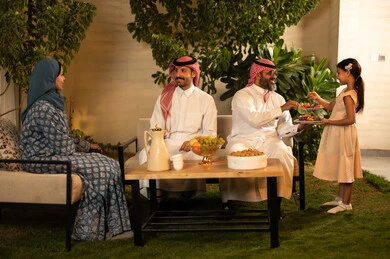 صلة الرحم والترابط الاسري, فرحة وبهجة الابناء في ايام العيد السعيد, التجمعات والزيارات الاسرية في الأعياد والمناسبات الاسلامية, عائلة عربية خليجية سعودية تجلس في الخارج ببإيماءات الفرح والسرور، ضيافة وحلوى العيد، حسن استقبال وإكرام الضيف