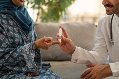 الفحوصات الطبية السريعة لمعرفة نسبة السكر في الدم، استخدام الأجهزة الالكترونية للتحاليل المنزلية، شابة سعودية مصابة بحالة مرضية مزمنة, طبيب عربي خليجي سعودي يرتدي المعطف الطبي يقوم بوخز اصبع امرأة, المتابعة الدورية لمرضى داء السكري