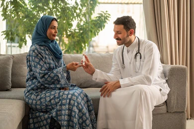 المتابعة الدورية لمرضى داء السكري, الفحوصات الطبية السريعة لمعرفة نسبة السكر في الدم، استخدام الأجهزة الالكترونية للتحاليل المنزلية، شابة سعودية مصابة بحالة مرضية مزمنة, طبيب عربي خليجي سعودي يرتدي المعطف الطبي يقوم بوخز اصبع امرأة