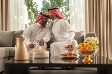 Getting satisfaction, the concept of love and tenderness, the role of the father in the lives of his children, a Saudi Arabian Gulf man wearing the traditional thobe and shemagh kissing his father's head, spending a fun and entertaining time, gestures of happiness and pleasure, a family atmosphere full of joy