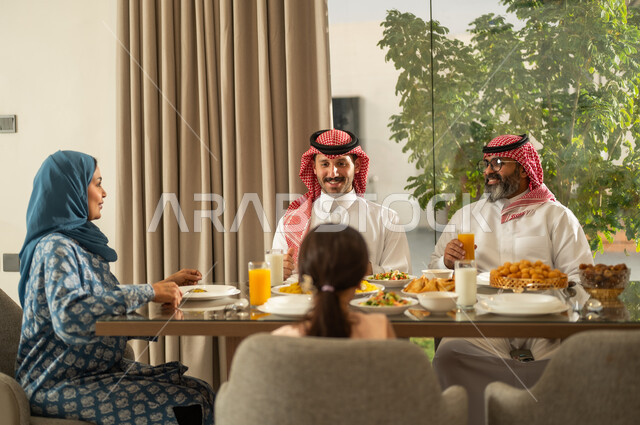  اجتماع الأسرة حول مائدة الإفطار المليئة بأصناف المأكولات والمقبلات الشهية، موعد كسر الصيام عند أذان المغرب في رمضان المبارك، فطور رمضاني عائلي، عائلة عربية خليجية سعودية تجلس بايماءات السرور, حسن الضيافة وإكرام الأخرين, أجواء عائلية روحانية دينية إسلامية