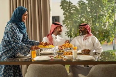 Family gathering around the Iftar table filled with delicious food and appetizers, the time to break the fast at sunset in the holy month of Ramadan, a family Ramadan Iftar, a Saudi Arabian Gulf family sitting with gestures of joy, good hospitality and honoring others, a spiritual, religious, Islamic family atmosphere