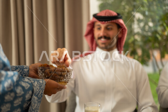  كسر الصيام بالتمر عند أذان المغرب في رمضان المبارك، فطور رمضاني عائلي، عائلة عربية خليجية سعودية تجلس بايماءات السرور, حسن الضيافة وإكرام الأخرين, أجواء عائلية روحانية دينية إسلامية, اجتماع الأسرة حول مائدة الإفطار المليئة بأصناف المأكولات والمقبلات الشهية