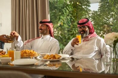 Breaking the fast with dates at the Maghrib call to prayer in the holy month of Ramadan, a family Ramadan breakfast, a Saudi Arabian Gulf family sitting with gestures of joy, good hospitality and honoring others, a spiritual, religious, Islamic family atmosphere, the family gathering around the breakfast table filled with delicious food and appetizers