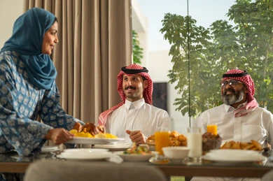 The time to break the fast is at sunset in the holy month of Ramadan, a family Ramadan breakfast, a Saudi Arabian Gulf family sitting with gestures of joy, good hospitality and honoring others, a spiritual, religious, Islamic family atmosphere, the family gathering around the breakfast table filled with delicious food and appetizers