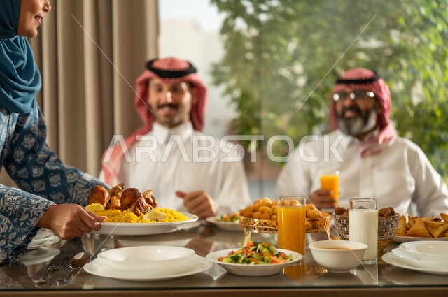  اجتماع الأسرة حول مائدة الإفطار المليئة بأصناف المأكولات والمقبلات الشهية، موعد كسر الصيام عند أذان المغرب في رمضان المبارك، فطور رمضاني عائلي، عائلة عربية خليجية سعودية تجلس بايماءات السرور, حسن الضيافة وإكرام الأخرين, أجواء عائلية روحانية دينية إسلامية