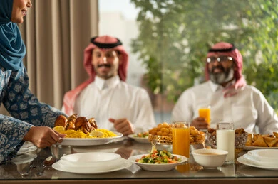 Family gathering around the Iftar table filled with delicious food and appetizers, the time to break the fast at sunset in the holy month of Ramadan, a family Ramadan Iftar, a Saudi Arabian Gulf family sitting with gestures of joy, good hospitality and honoring others, a spiritual, religious, Islamic family atmosphere