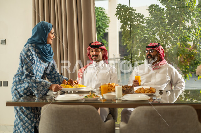  اجتماع الأسرة حول مائدة الإفطار المليئة بأصناف المأكولات والمقبلات الشهية، موعد كسر الصيام عند أذان المغرب في رمضان المبارك، فطور رمضاني عائلي، عائلة عربية خليجية سعودية تجلس بايماءات السرور, حسن الضيافة وإكرام الأخرين, أجواء عائلية روحانية دينية إسلامية