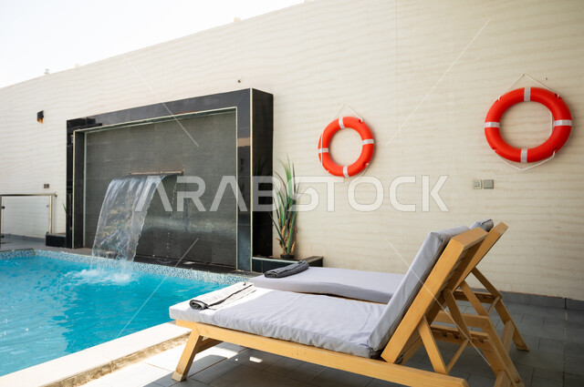 A quiet outdoor seating area in front of the swimming pool, luxurious home furnishings in a chalet, modern interior design for seating areas, suites furnished with all the finest furnishings, elegant interior design for villas and residential apartments in the Kingdom of Saudi Arabia.