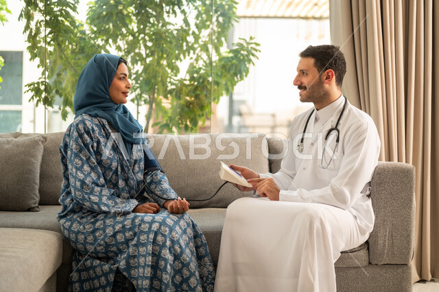 استخدام الميزان الالكتروني الحديث والمتطور للفحص المنزلي السريع,  طبيب عربي خليجي سعودي يرتدي المعطف الطبي يقوم بقياس ضغط الدم للمريضة في المنزل, مفهوم الرعاية الصحية والاهتمام بالصحة الجسدية
