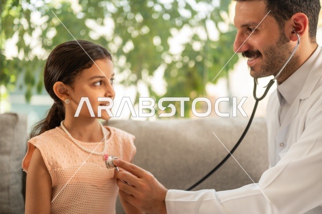 العمل في القطاع الصحي في السعودية،  القيام بالرعاية الصحية والاهتمام بصحة المرضى، طبيب عربي خليجي سعودي يرتدي الثوب التقليدي يقوم بفحص فتاة عبر سماعة الأذن في المنزل، استخدام سماعة الطبيب لسماع نبضات القلب
