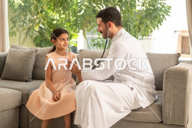 العمل في القطاع الصحي في السعودية،  القيام بالرعاية الصحية والاهتمام بصحة المرضى، طبيب عربي خليجي سعودي يرتدي الثوب التقليدي يقوم بفحص فتاة عبر سماعة الأذن في المنزل، استخدام سماعة الطبيب لسماع نبضات القلب