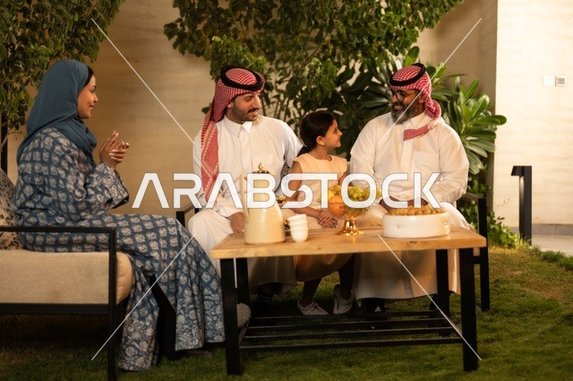 ضيافة وحلوى العيد، حسن استقبال وإكرام الضيف، صلة الرحم والترابط الاسري, فرحة وبهجة الابناء في ايام العيد السعيد, التجمعات والزيارات الاسرية في الأعياد والمناسبات الاسلامية, رجل عربي خليجي سعودي يرتدي الثوب التقليدي يجلس مع أحفاده بإيماءات الفرح والسرور